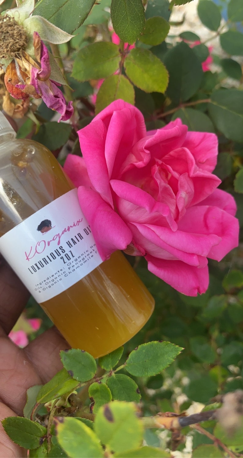 May include: A clear glass bottle with a yellow liquid inside. The bottle has a white label with black text that reads "KOrganix Luxurious Hair Oil 201 Ingredients: Organic Oils Organic Fenugreek & Organic Chamomile"