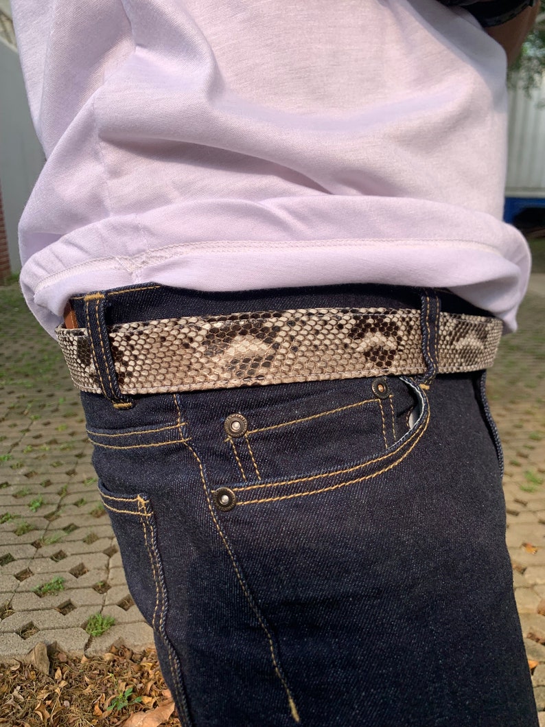 May include: A dark blue denim jean with a snakeskin belt. The belt is brown and white with a textured pattern.