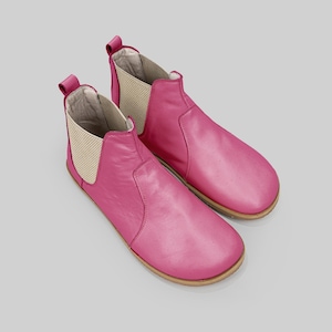 May include: A pair of bright pink Chelsea boots. The boots have a smooth leather upper, elastic side panels, and a pull tab at the back. The soles are a light brown color.