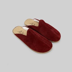 Pode incluir: Um par de chinelos de camurça bordô. Os chinelos têm bico arredondado e design slip-on. O interior é forrado com um material de cor clara e as solas são de cor natural. Os chinelos são projetados para uso interno.