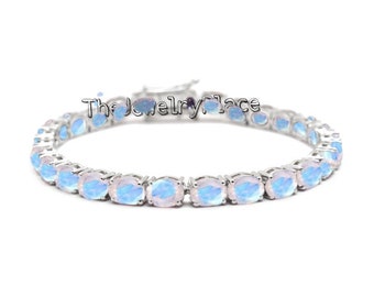 Puede incluir: Un brazalete de tenis de plata con opales azules de forma ovalada. El brazalete está hecho de plata de ley y tiene un cierre seguro.