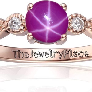 May include: A rose gold ring with a pink star sapphire gemstone and three smaller diamonds. The ring is engraved with "The Jewelry Place".