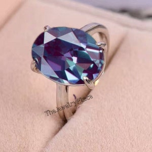 Può includere: Un anello d'argento con una grande pietra preziosa ovale e iridescente. La pietra preziosa è di colore blu, viola e verde.