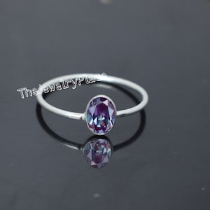 Op de afbeelding: Een zilveren ring met een paarse ovale edelsteen. De edelsteen heeft een regenboog effect.