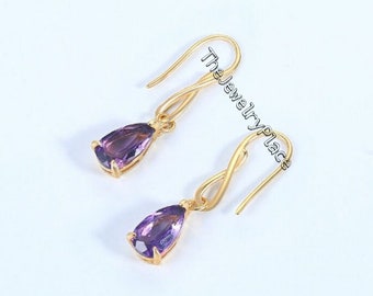 May include: A pair of gold dangle earrings with purple pear-shaped gemstones. The earrings have a twisted wire design.