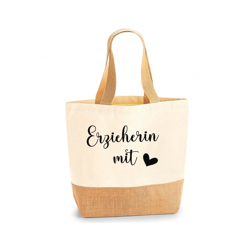 May include: A beige tote bag with a natural jute bottom and handles. The bag features the text "Erzieherin mit" and a black heart symbol. The bag is designed for carrying items.