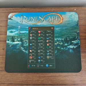 Può includere: Tappetino per mouse rettangolare con il logo Runescape e un'interfaccia di gioco con livelli di abilità. Lo sfondo raffigura un paesaggio fantasy con montagne e una torre. Per uso informatico.