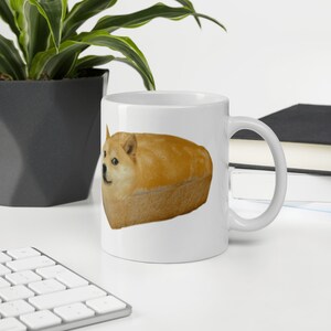 May include: White ceramic mug with a printed image of a Shiba Inu dog inside a loaf of bread. The dog's face is visible and the bread is brown.