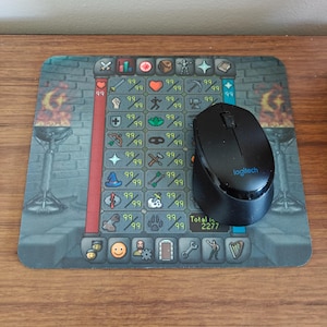 Puede incluir: Alfombrilla de ratón rectangular con un diseño de interfaz de videojuego, que muestra varios iconos y el número "99". Un ratón inalámbrico negro Logitech descansa sobre ella. El total es 2277.