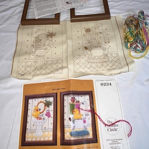 May include: A cross-stitch kit titled "0234 Bath Time" featuring two framed designs of a duck in a bathroom setting. The kit includes printed fabric, wool yarns, and instructions. The finished size is 7" x 7" (17.7 cm x 17.7 cm).