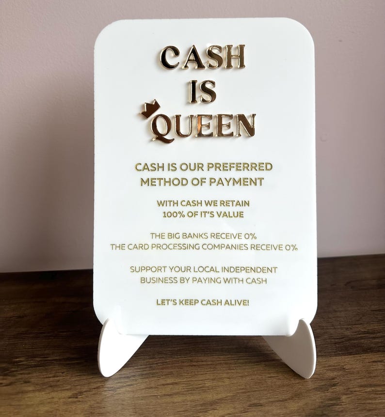 May include: White sign with gold lettering that reads "CASH IS QUEEN". The sign also includes the text "CASH IS OUR PREFERRED METHOD OF PAYMENT. WITH CASH WE RETAIN 100% OF IT'S VALUE. THE BIG BANKS RECEIVE 0%. THE CARD PROCESSING COMPANIES RECEIVE 0%. SUPPORT YOUR LOCAL INDEPENDENT BUSINESS BY PAYING WITH CASH. LET'S KEEP CASH ALIVE!"