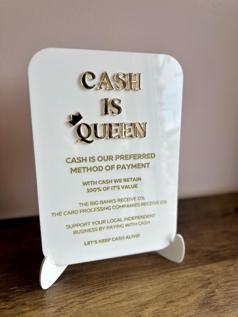 May include: White sign with gold lettering that reads "Cash is Queen". The sign also includes the text "Cash is our preferred method of payment. With cash we retain 100% of it's value. The big banks receive 0%. The card processing companies receive 0%. Support your local independent business by paying with cash. Let's keep cash alive."