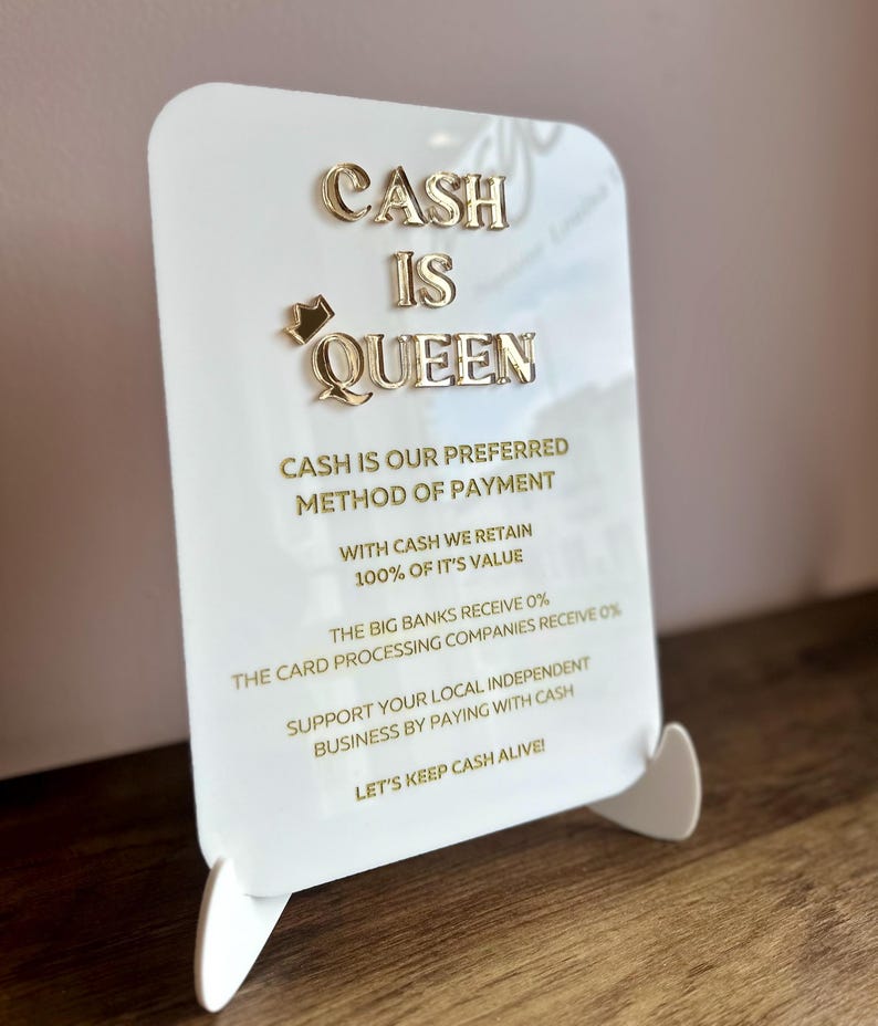 May include: White sign with gold lettering that reads "CASH IS QUEEN". The sign also includes the text "CASH IS OUR PREFERRED METHOD OF PAYMENT", "WITH CASH WE RETAIN 100% OF IT'S VALUE", "THE BIG BANKS RECEIVE 0%", "THE CARD PROCESSING COMPANIES RECEIVE 0%", "SUPPORT YOUR LOCAL INDEPENDENT BUSINESS BY PAYING WITH CASH", and "LET'S KEEP CASH ALIVE!"