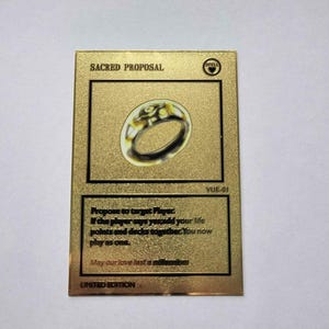 May include: A gold card with the text "SACRED PROPOSAL" and a gold ring with a diamond on it. The card also has the text "VUE-01" and "LIMITED EDITION".