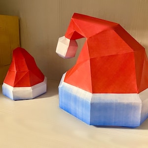 Può includere: Due cappelli di Babbo Natale di carta rossi e bianchi, uno più grande dell'altro, con bordino blu. Il cappello più grande è inclinato di lato.