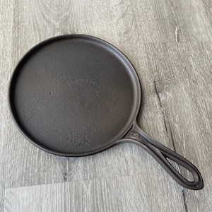May include: A black cast iron griddle with a long handle. The griddle is round and has a smooth surface.
