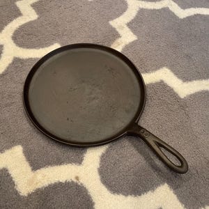 May include: A black cast iron griddle with a long handle. The griddle is round and has a smooth surface.