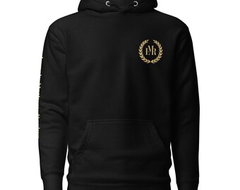May include: Black hoodie with a front pocket and a drawstring hood. The hoodie features a gold emblem on the chest and text on the left sleeve. The emblem is a laurel wreath with the letters "DR" inside. The text on the sleeve is also gold.