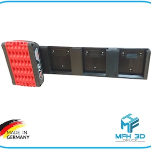 Könnte beinhalten: Eine schwarze, im 3D-Druck hergestellte Wandhalterung für die Aufbewahrung mehrerer 18V-Akkus. Die Halterung hat Steckplätze für vier Akkus und ein einzelner Akku ist in der Halterung zu sehen. Der Akku ist rot und schwarz mit dem aufgedruckten Text "18V".