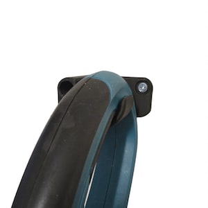 Pode incluir: Close-up de uma pega de ferramenta elétrica. A pega é uma combinação de plástico preto e verde-azulado. Uma pega preta está no topo da pega verde-azulado. Um suporte preto é fixado à pega com um parafuso.
