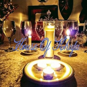 Puede incluir: Una mesa puesta con copas de vino, velas y un plato decorativo con tres velas de t&eacute; encendidas. Las velas est&aacute;n sobre un plato redondo de color dorado. La mesa est&aacute; cubierta con un mantel de color dorado.