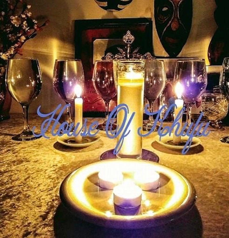Puede incluir: Una mesa puesta con copas de vino, velas y un plato decorativo con tres velas de t&eacute; encendidas. Las velas est&aacute;n sobre un plato redondo de color dorado. La mesa est&aacute; cubierta con un mantel de color dorado.