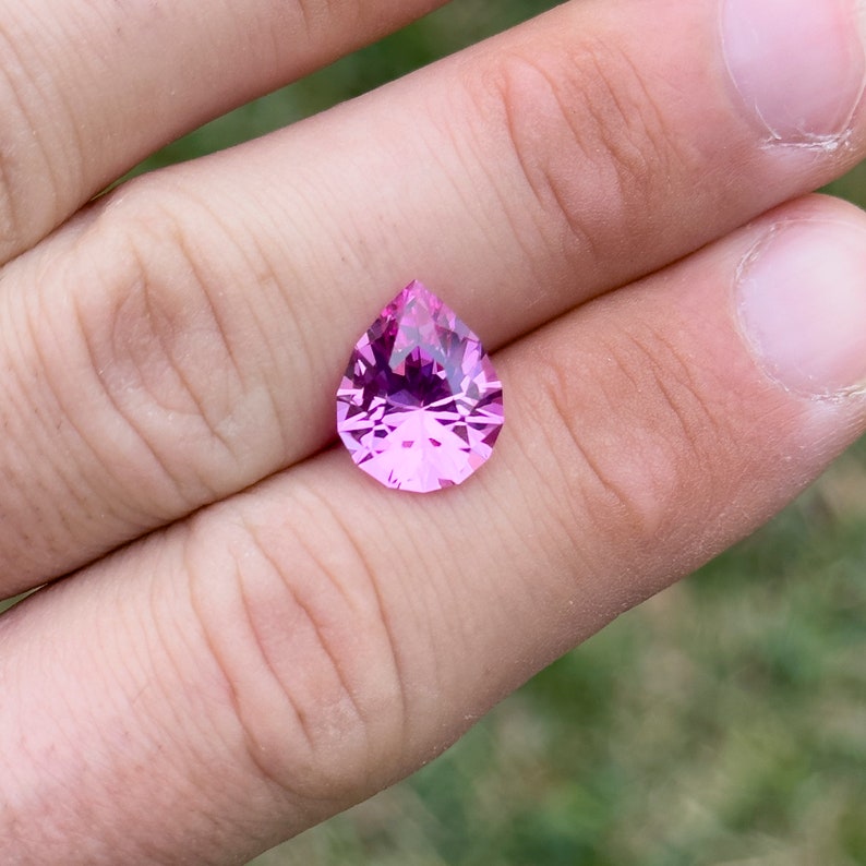 Puede incluir: Una piedra preciosa rosa en forma de pera con facetas, sostenida en una mano.