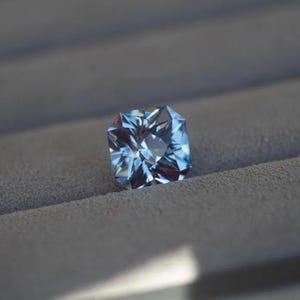 May include: A light blue gemstone with a square shape and many facets.