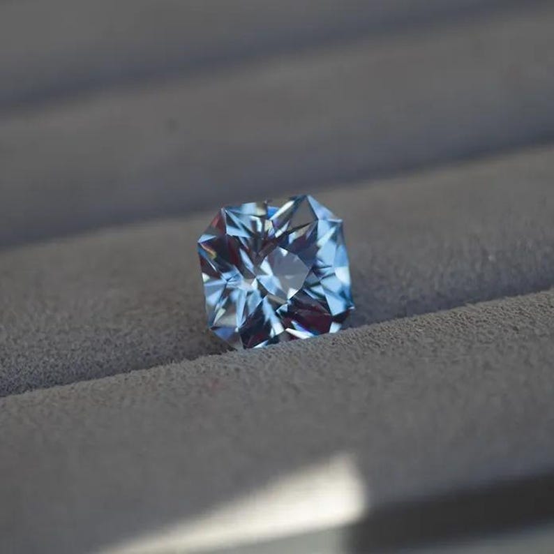 May include: A light blue gemstone with a square shape and many facets.