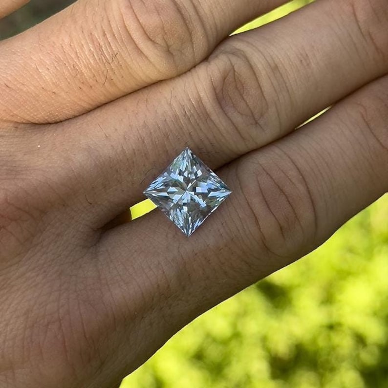 Op de afbeelding: Een heldere, vierkante edelsteen met een prinsessenslijp. De edelsteen is gezet in een ring en wordt aan een vinger gedragen.