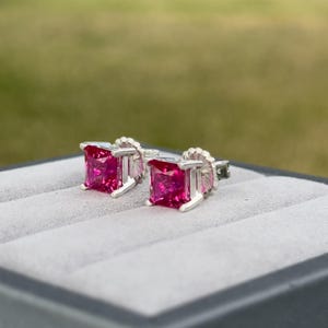 Puede incluir: Un par de pendientes de plata con piedras preciosas rosas de forma cuadrada.