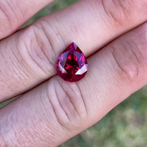 May include: A deep red pear-shaped gemstone with many facets.