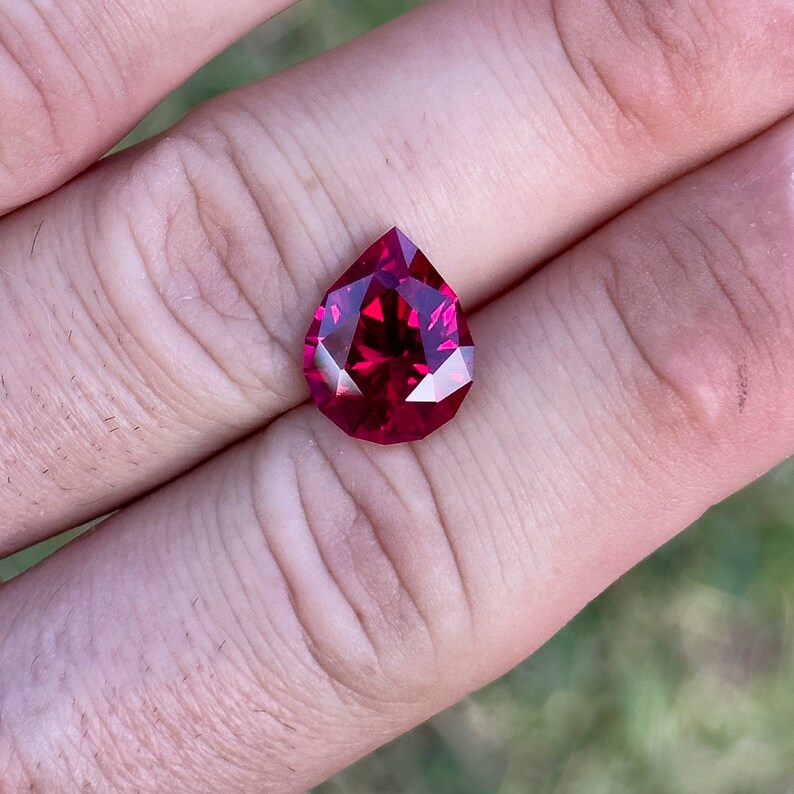 May include: A deep red pear-shaped gemstone with many facets.