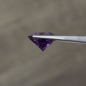 Op de afbeelding: Een paarse edelsteen met een facetgeslepen vorm, vastgehouden door een pincet.