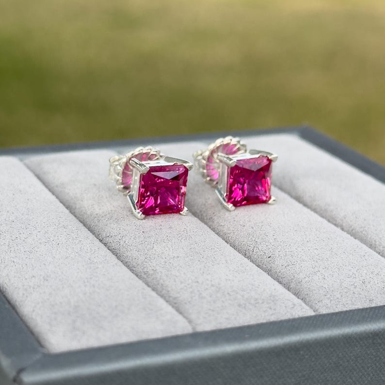 Puede incluir: Un par de pendientes de bot&oacute;n de plata con piedras preciosas cuadradas de color rosa.