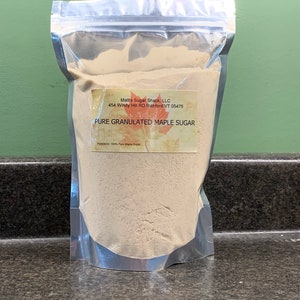 May include: A clear, sealed bag filled with pure granulated maple sugar. The bag has a label with the text "Matt's Sugar Shack, LLC" and "Pure Granulated Maple Sugar". The ingredients are listed as 100% pure maple sugar.