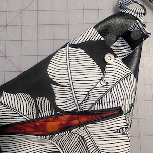 Op de afbeelding: Schoudertas met een zwart-wit bladpatroon. De tas heeft een zwarte rits, een zwart lederen detail en een magnetische sluiting. De binnenvoering is oranje en rood.