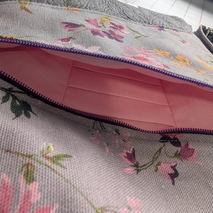 Front pocket with card slots. . Left shoulder, light grey with floral print bag with matching strap and soft, grey faux leather accents.