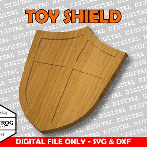 May include: A wooden shield with a carved design. The shield is light brown and has a slightly curved shape. The text "TOY SHIELD" is printed in orange letters at the top of the image.