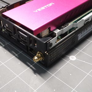 May include: A black computer component housing with a bright pink Yeston branded cover plate. The unit features a gold-colored antenna connector port on the side, exposed internal circuitry, and a black metal frame with ventilation perforations.