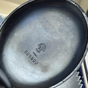 May include: The interior of a dark metallic pocket watch case featuring a circular emblem with the text Ulysse Nardin Le Locle, the word Swiss, and the engraved serial number 605802 centered on the smooth, slightly tarnished dark grey surface.
