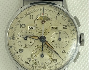 Puede incluir: Un reloj de pulsera cronógrafo Universal Geneve plateado con una esfera blanca y una correa de cuero negra. El reloj tiene tres subesferas, una ventana de fecha y un indicador de fase lunar. La esfera del reloj también incluye el texto "Universal Geneve" y "Tri-Com."