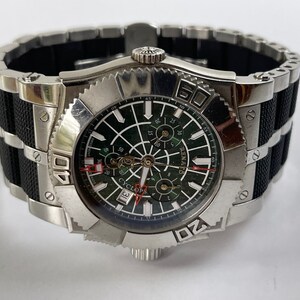 May include: A silver and black wristwatch with a green face and a black rubber strap. The watch has a date window and a chronograph function. The face of the watch has the word "Cyclops" printed on it.