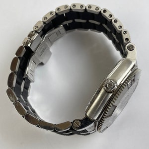 May include: A silver wristwatch with a black rubber strap. The watch has a round face with a silver bezel and a silver strap.