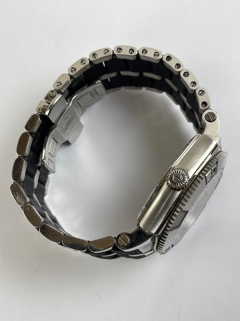 May include: A silver wristwatch with a black rubber strap. The watch has a round face with a silver bezel and a silver strap.