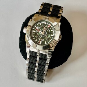May include: A silver and black wristwatch with a green face and a black rubber strap. The watch has a chronograph function and a date window. The watch face has the word "CHRONO" printed on it.