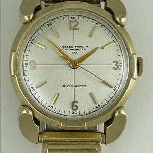 May include: A gold-toned wristwatch with a white face and black hands. The watch face has the text "Ulysse Nardin Chronometer Co." and "Automatic".