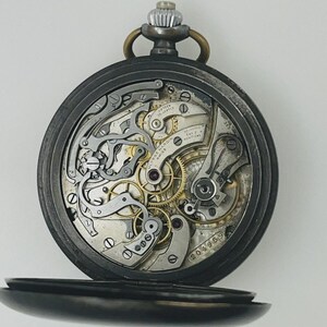 May include: A pocket watch with an open back revealing the intricate silver and gold-toned mechanical movement. The internal plate is engraved with Ulysse Nardin Swiss, fifteen jewels, adjusted to two positions, and the serial number 204959.