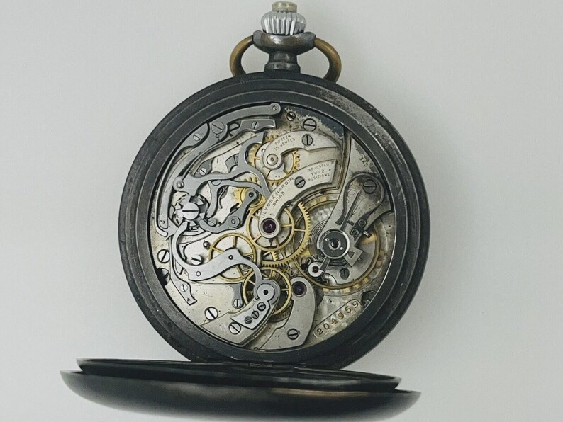 May include: A pocket watch with an open back revealing the intricate silver and gold-toned mechanical movement. The internal plate is engraved with Ulysse Nardin Swiss, fifteen jewels, adjusted to two positions, and the serial number 204959.