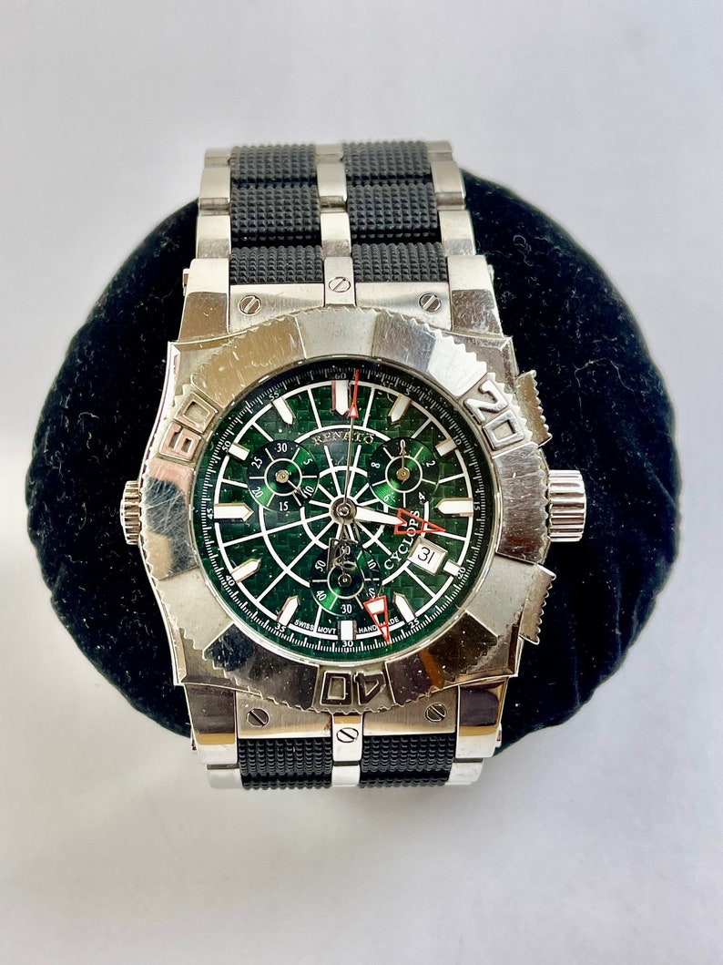 May include: A silver and black wristwatch with a green face and a black rubber strap. The face has a cyclops date window and the text "RENATO CYCLOPS" printed on it.